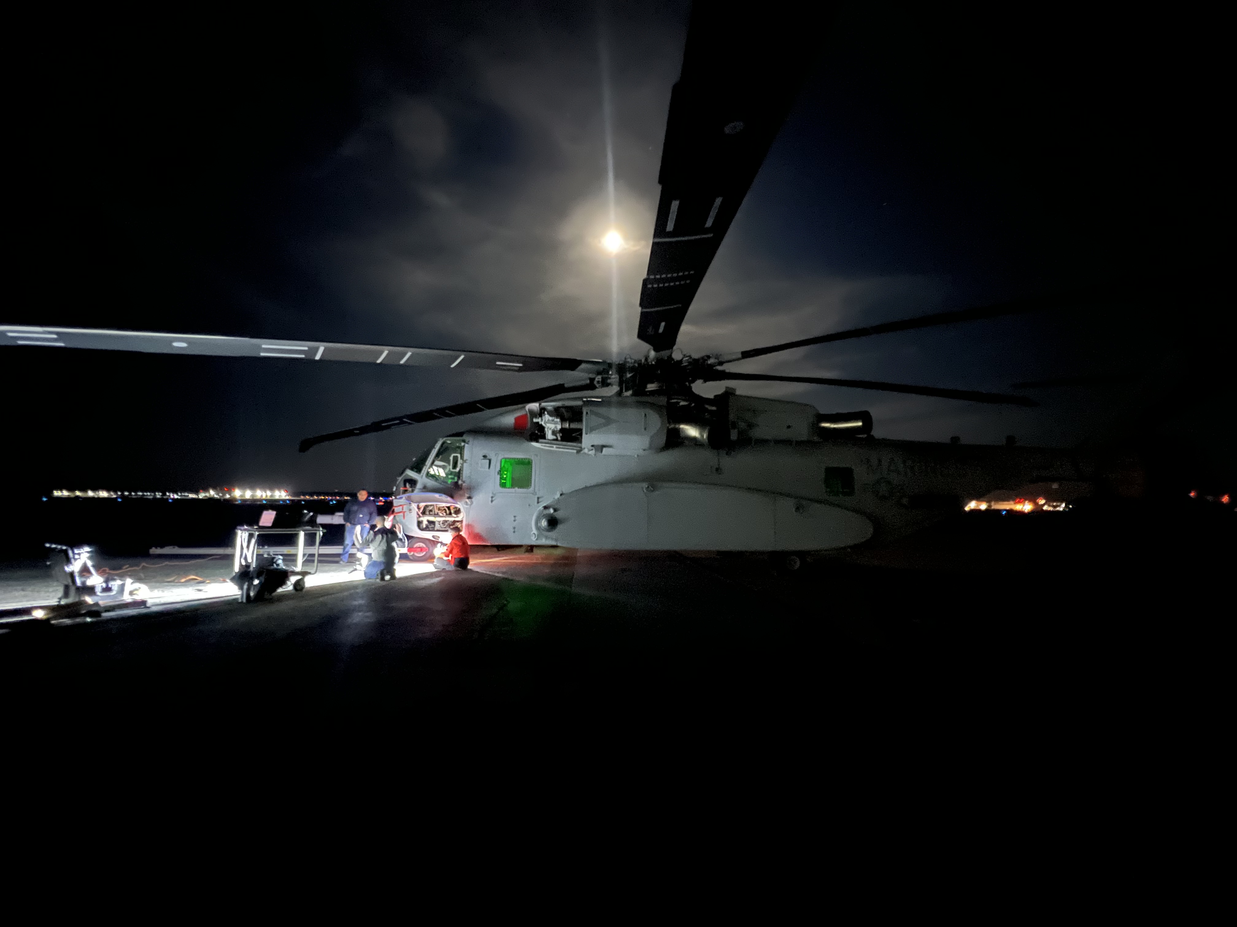 Helicopter sits on a dark runway with the moon shining overhead