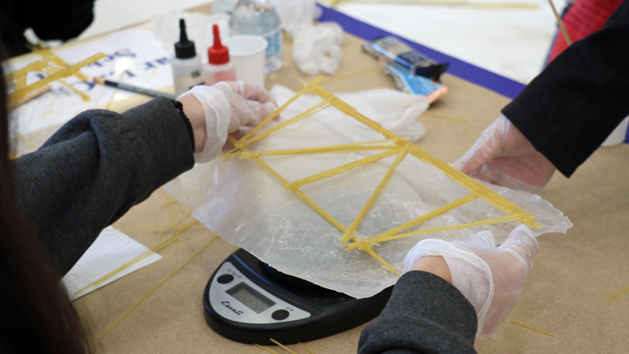 Students participating in the annual Tri-Warfare Center STEM Challenge in Point Mugu, California, on Feb. 20 weigh their spaghetti bridge, which could not weigh more than 50 grams. (U.S. Navy photo by Kimberly Brown)