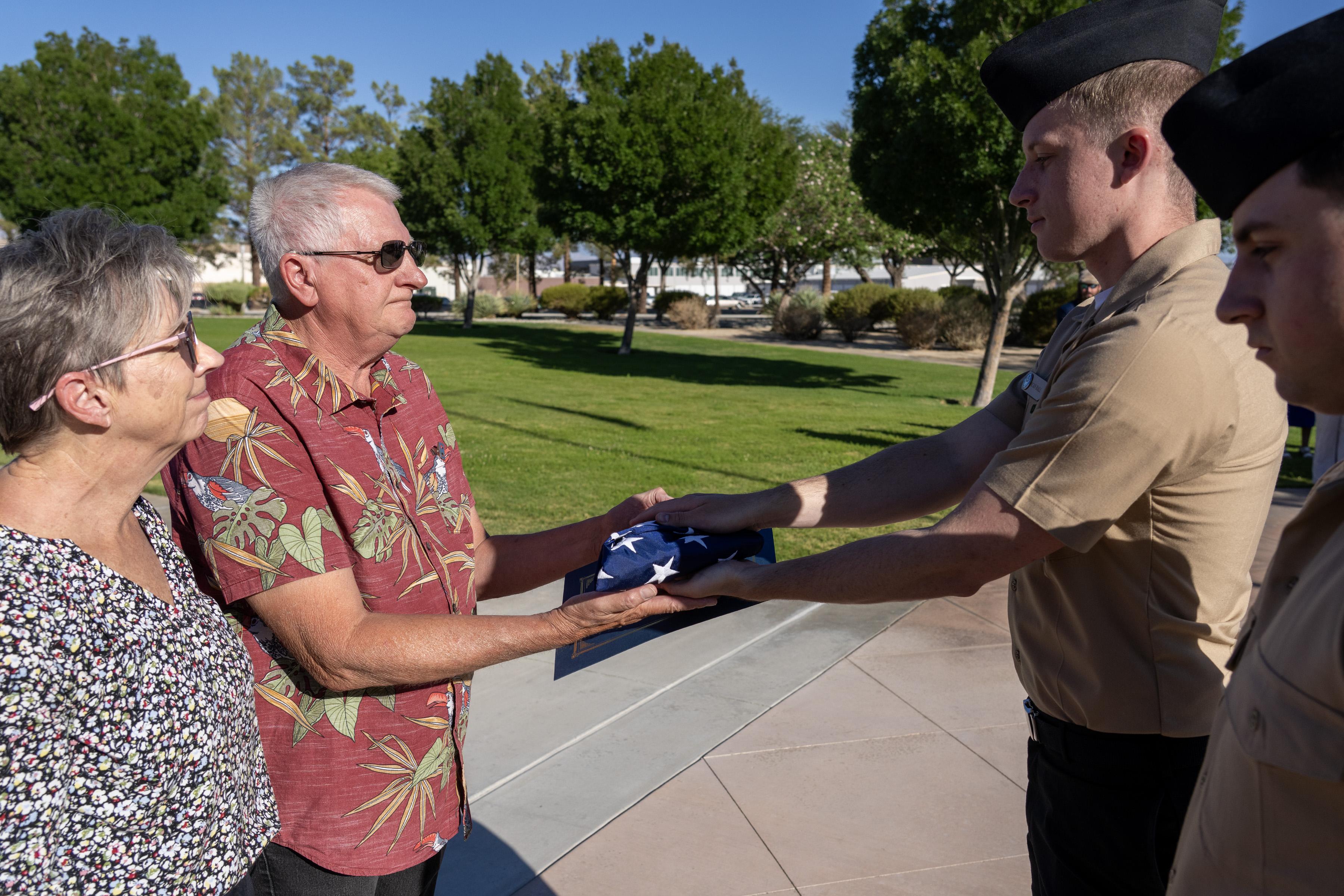 Harlan Kooima, (center) director of research and development at Naval Air Warfare Center Weapons Division alongside his wife, Kim, is presented with a flag during a ceremony celebrating his retirement from federal service on July 31 in China Lake, Calif. 