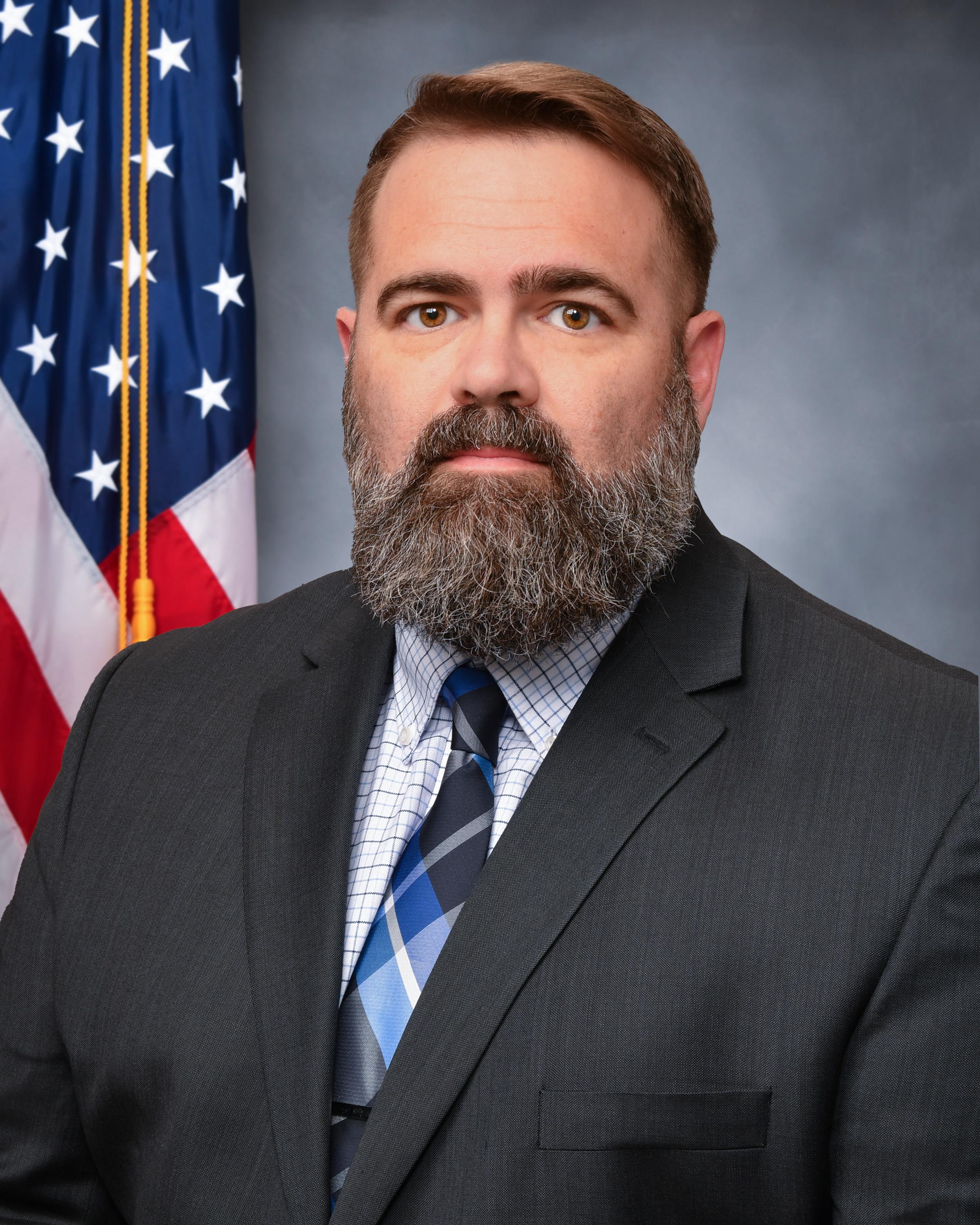 Professional headshot of man wearing a suit with the American flag in background 