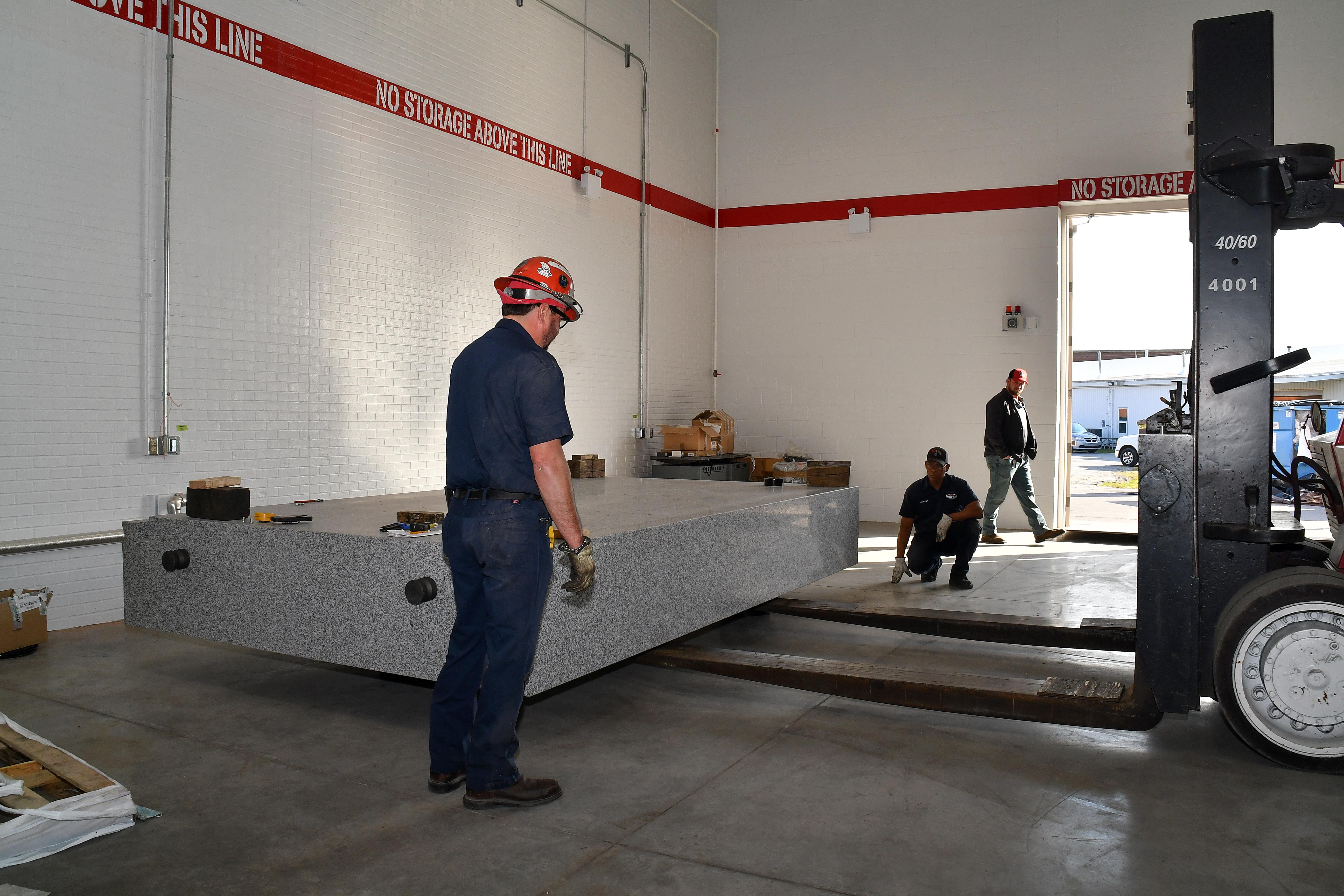 Rigging technicians move a granite table weighing 14 tons into place at Fleet Readiness Center East (FRCE). The table is part of a coordinate measuring machine (CMM). FRCE recently acquired two new CMMs capable of large-volume measurement. In addition to providing large item measurements, depot officials say these additional machines will improve efficiency and reduce wait times caused by maintenance and equipment calibration.