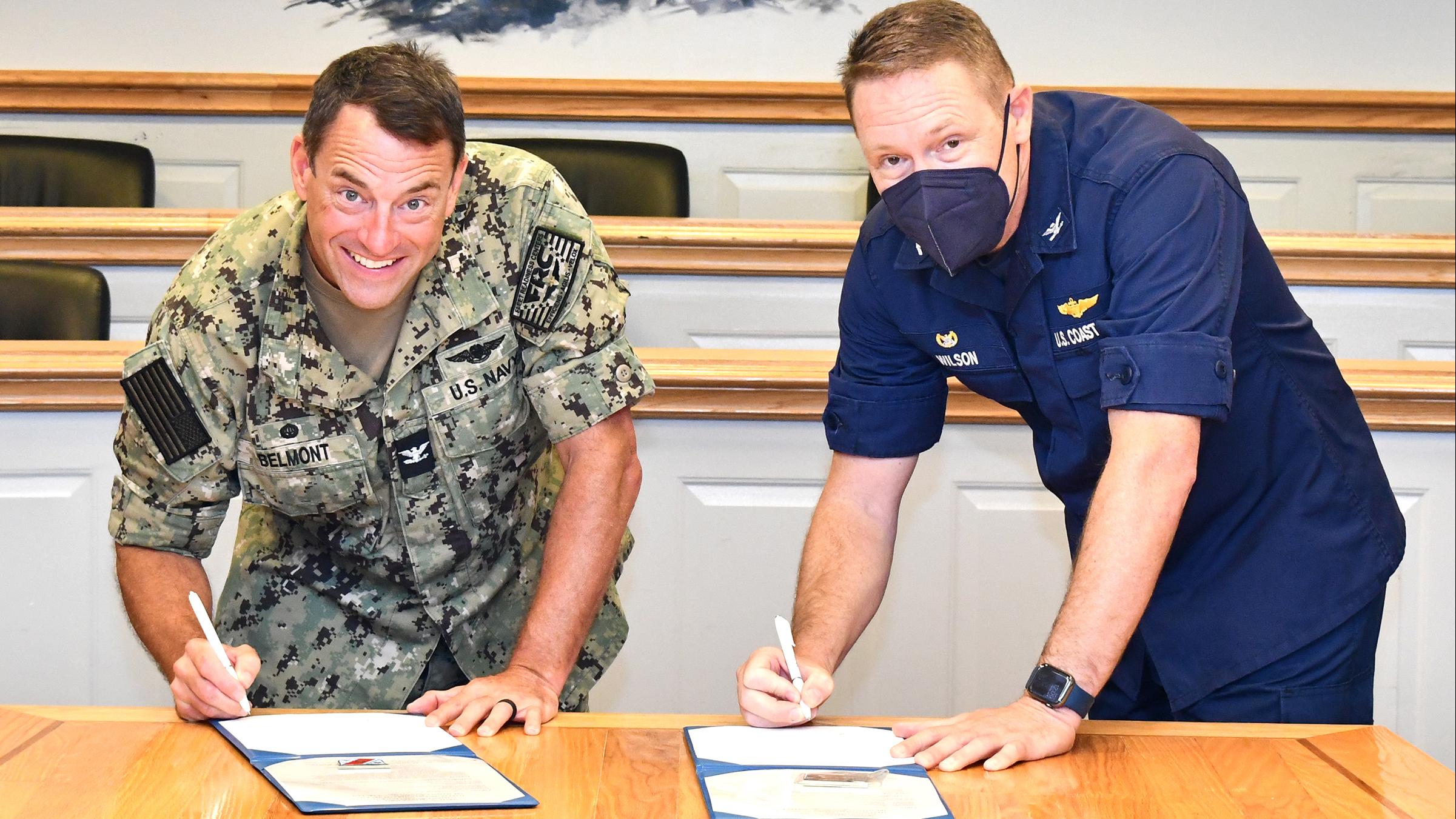 Two commanders look at camera while signing documents