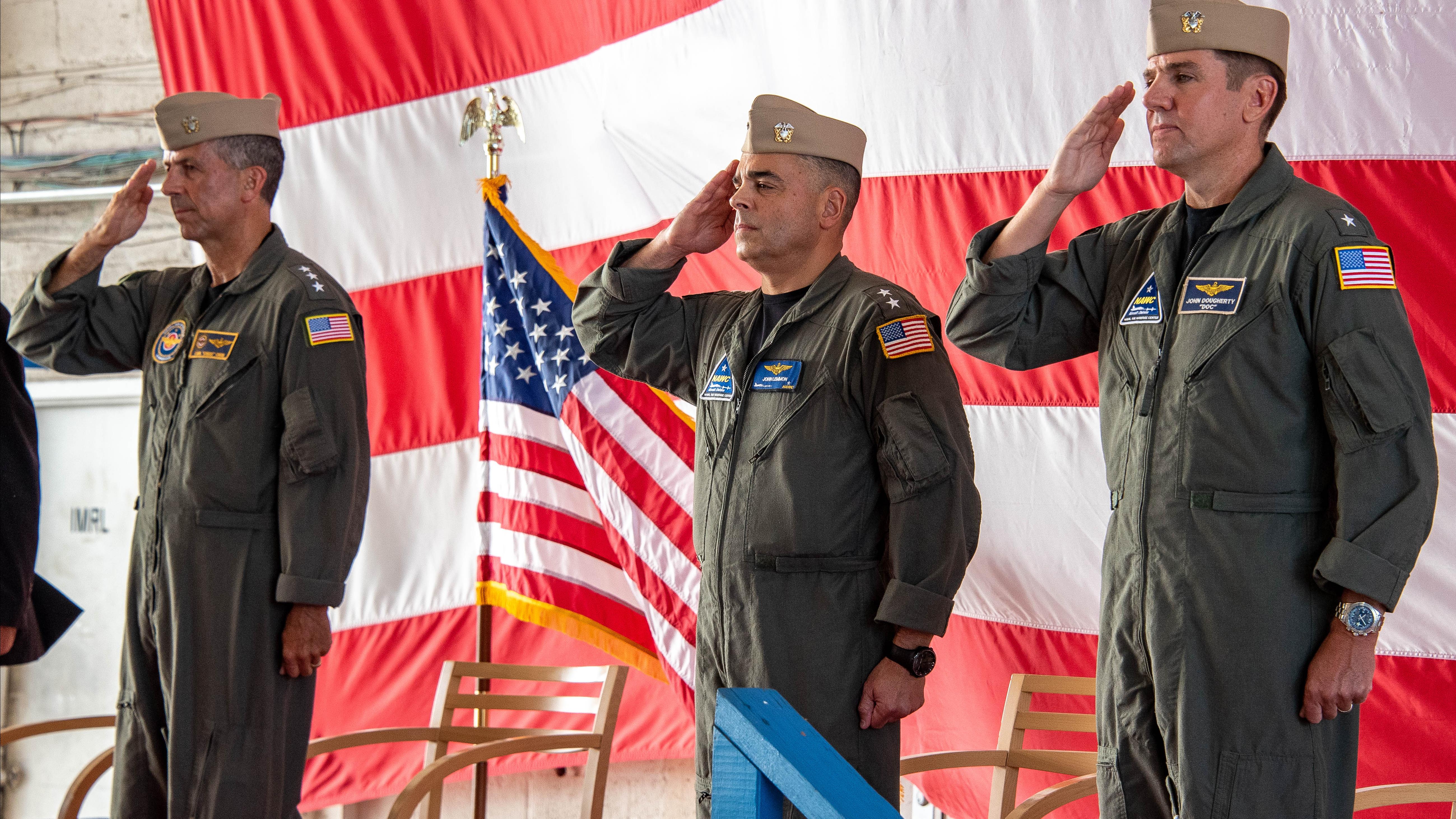 NAVAIR's Vice Adm. Carl Chebi, outgoing Rear Adm. John Lemmon, and incoming Rear Adm. John Dougherty IV salute in front of the American flag.