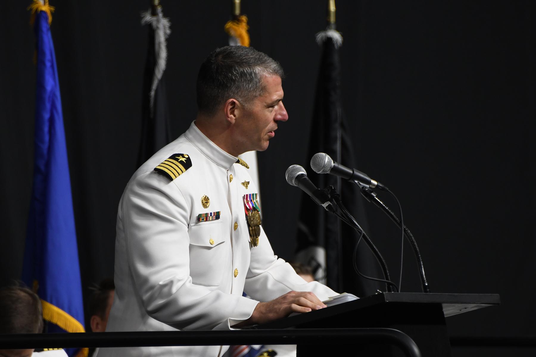 Navy captain in uniform speaking at podium. 