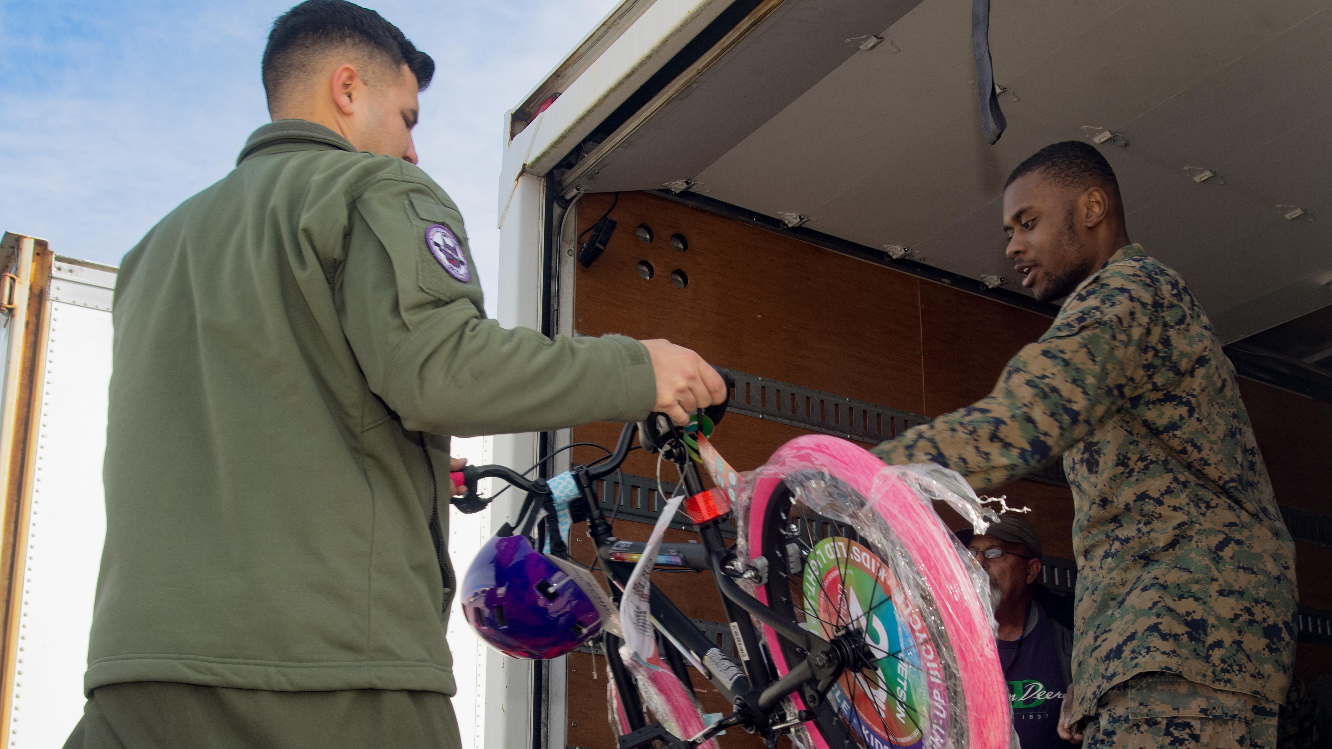 Man handing another man a children's bike with pink tires. 