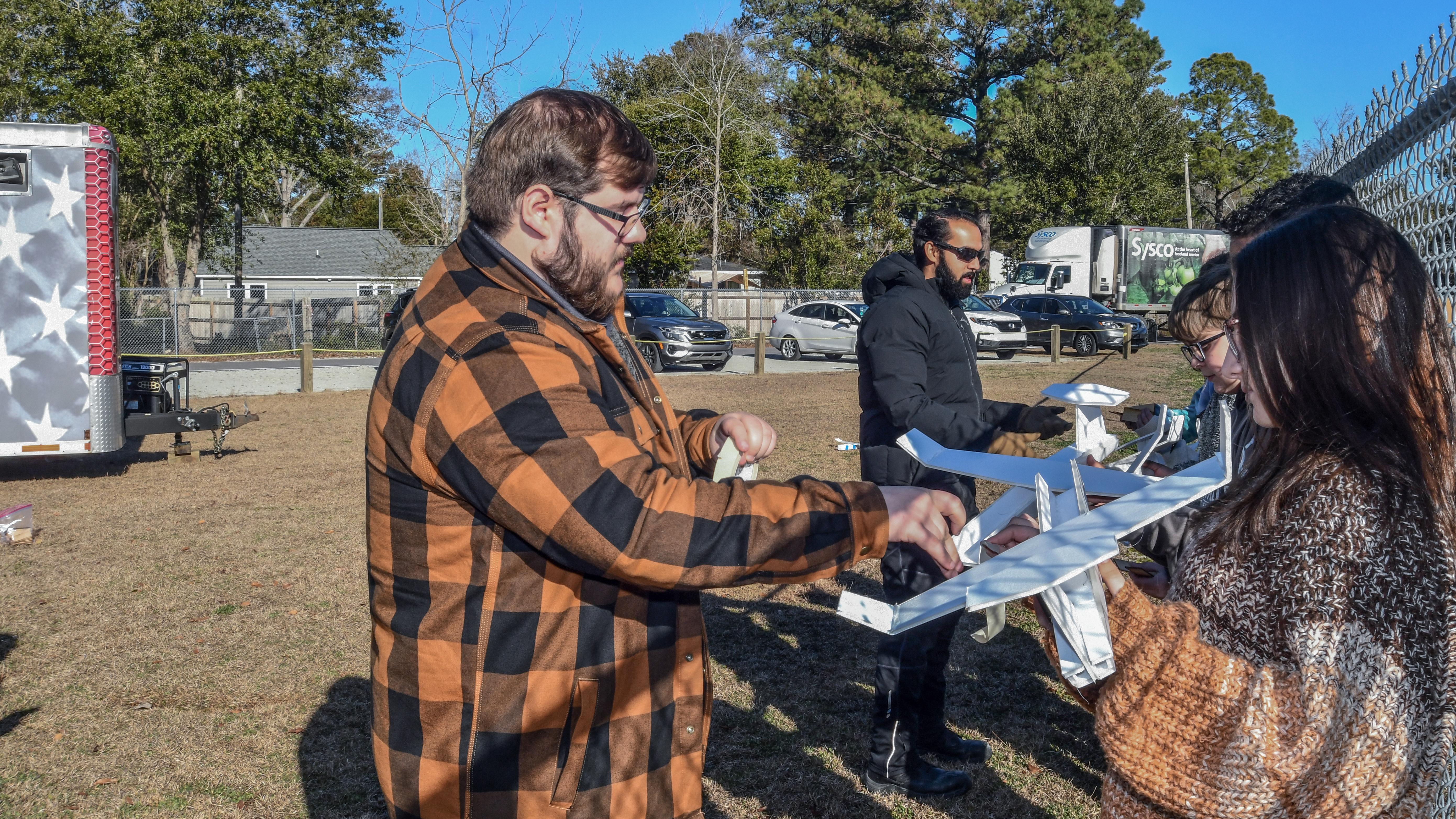 Man stands on the left helping female student on the right with foam airplane