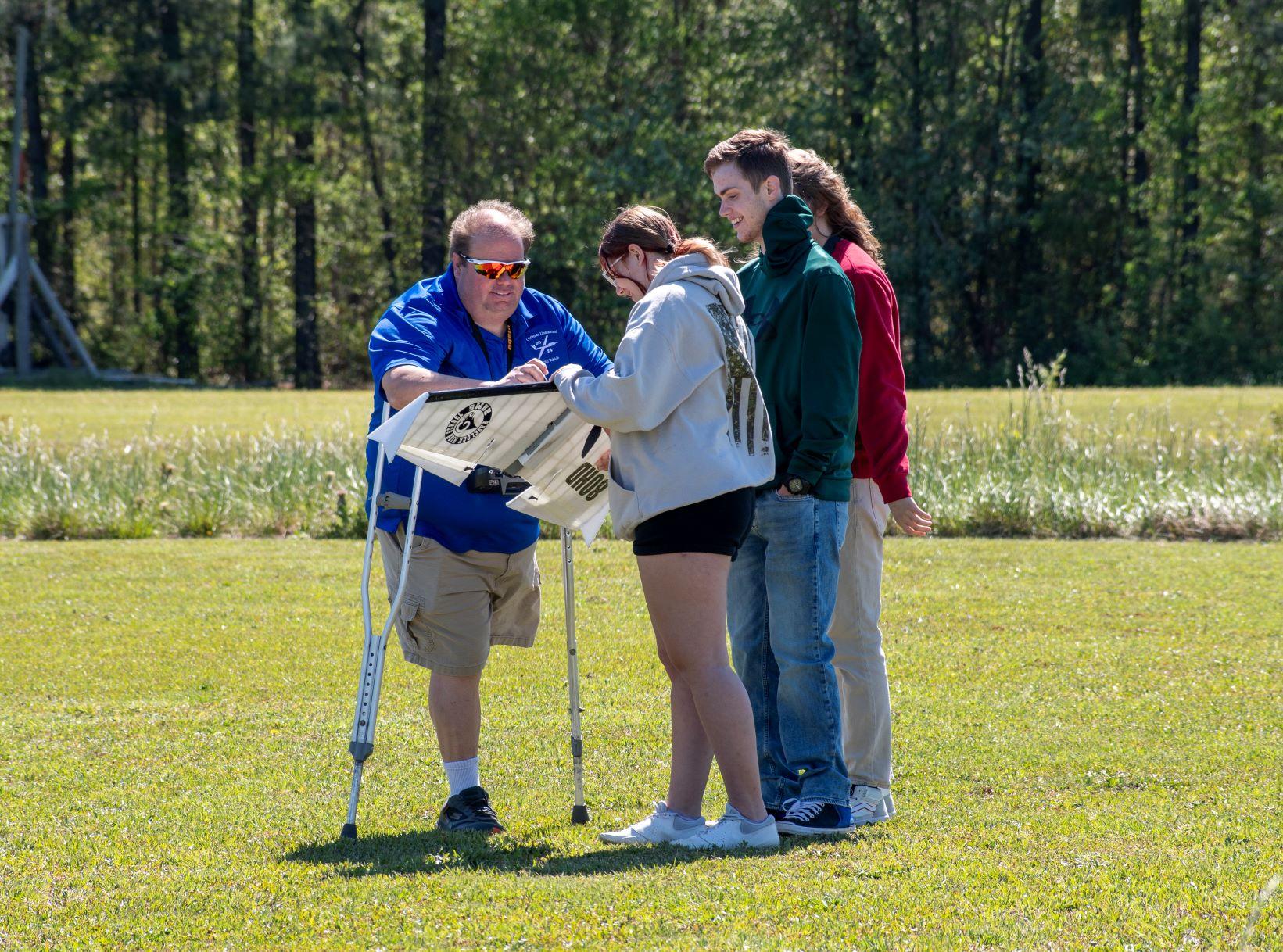 Three students stand with a gentleman on crutches outside 