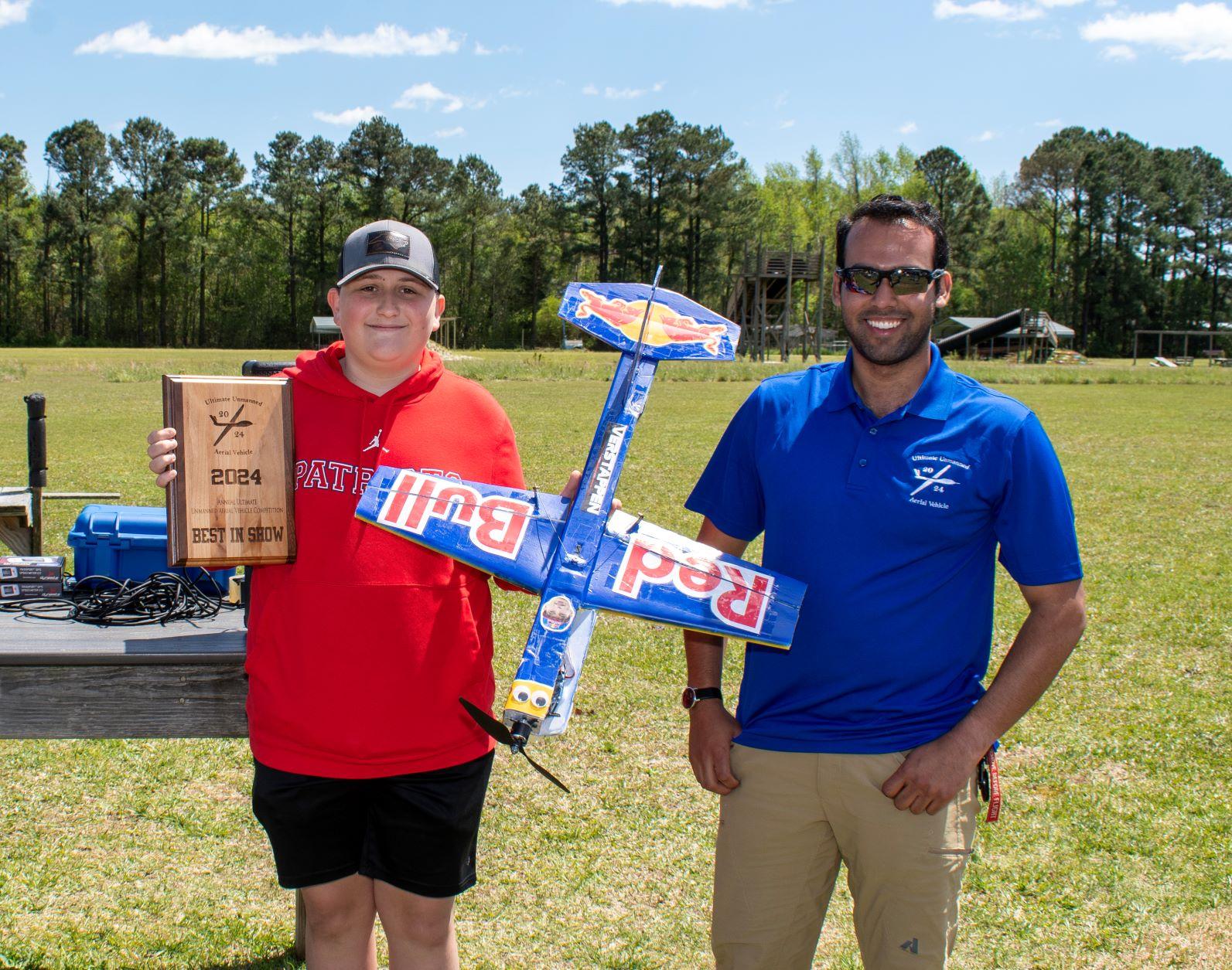 Student holds model aircraft and plaque next to a gentleman in blue 