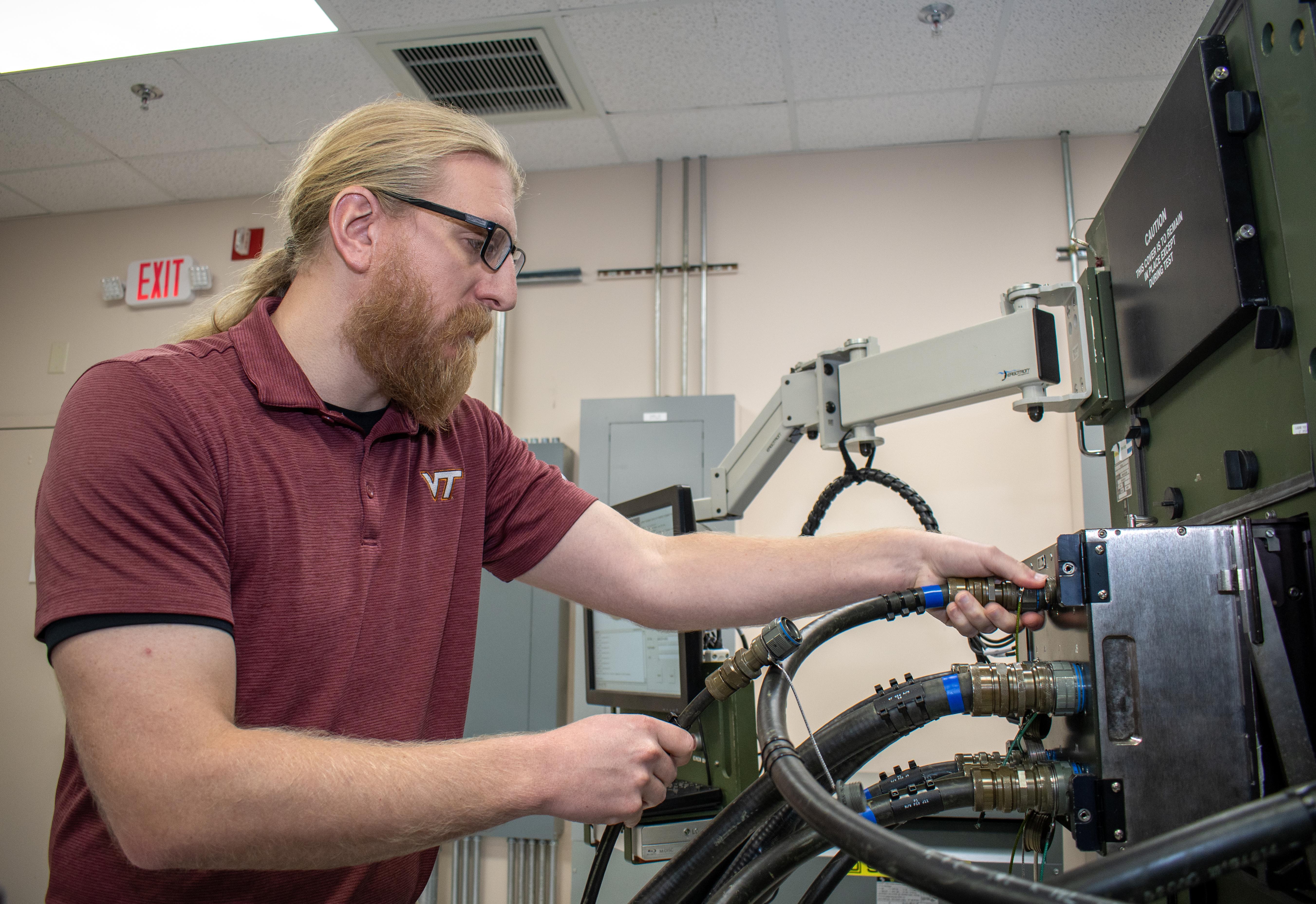 Man in red shirt plugging large cords into machine 