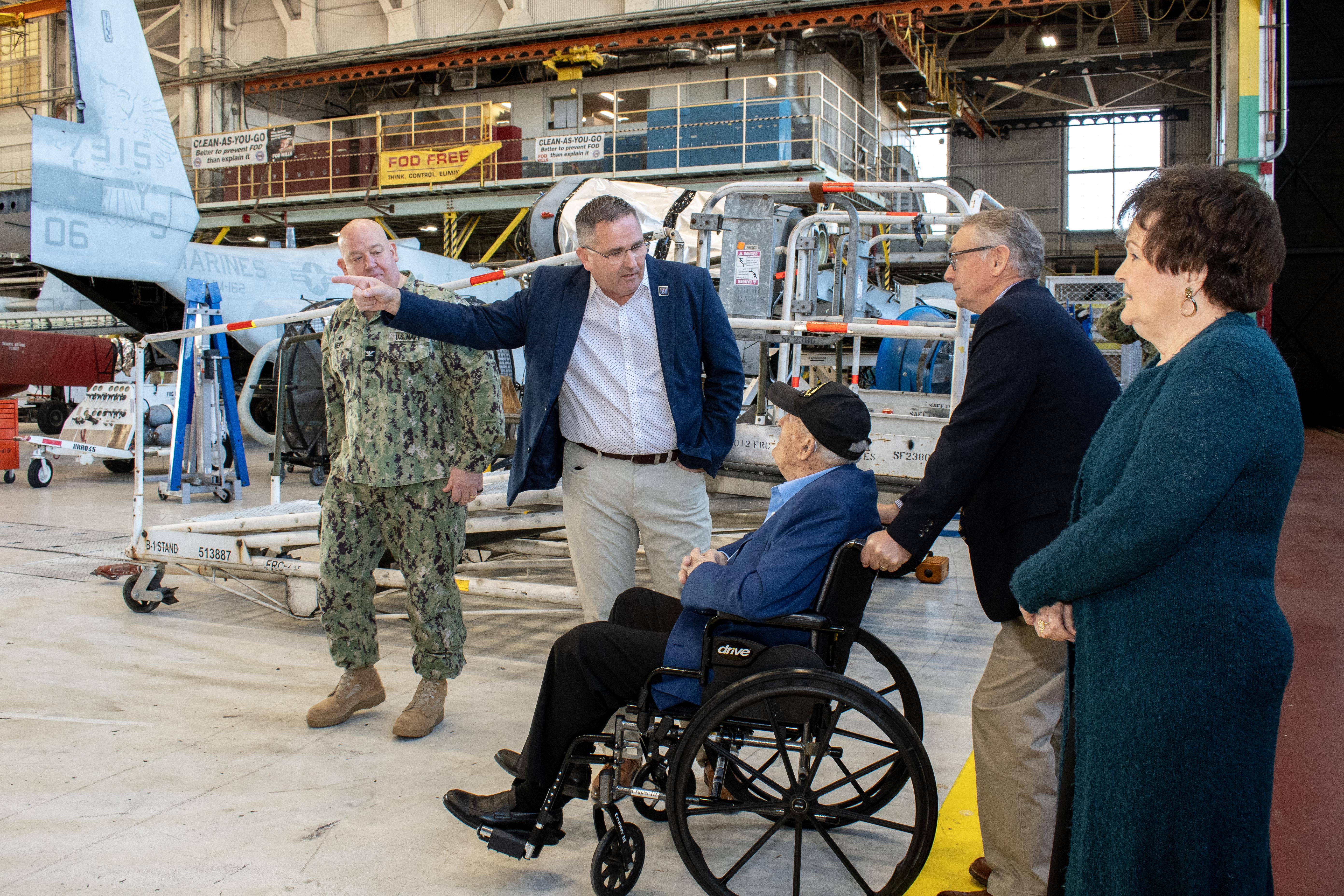 Four people standing and one person in wheelchair in aircraft hangar