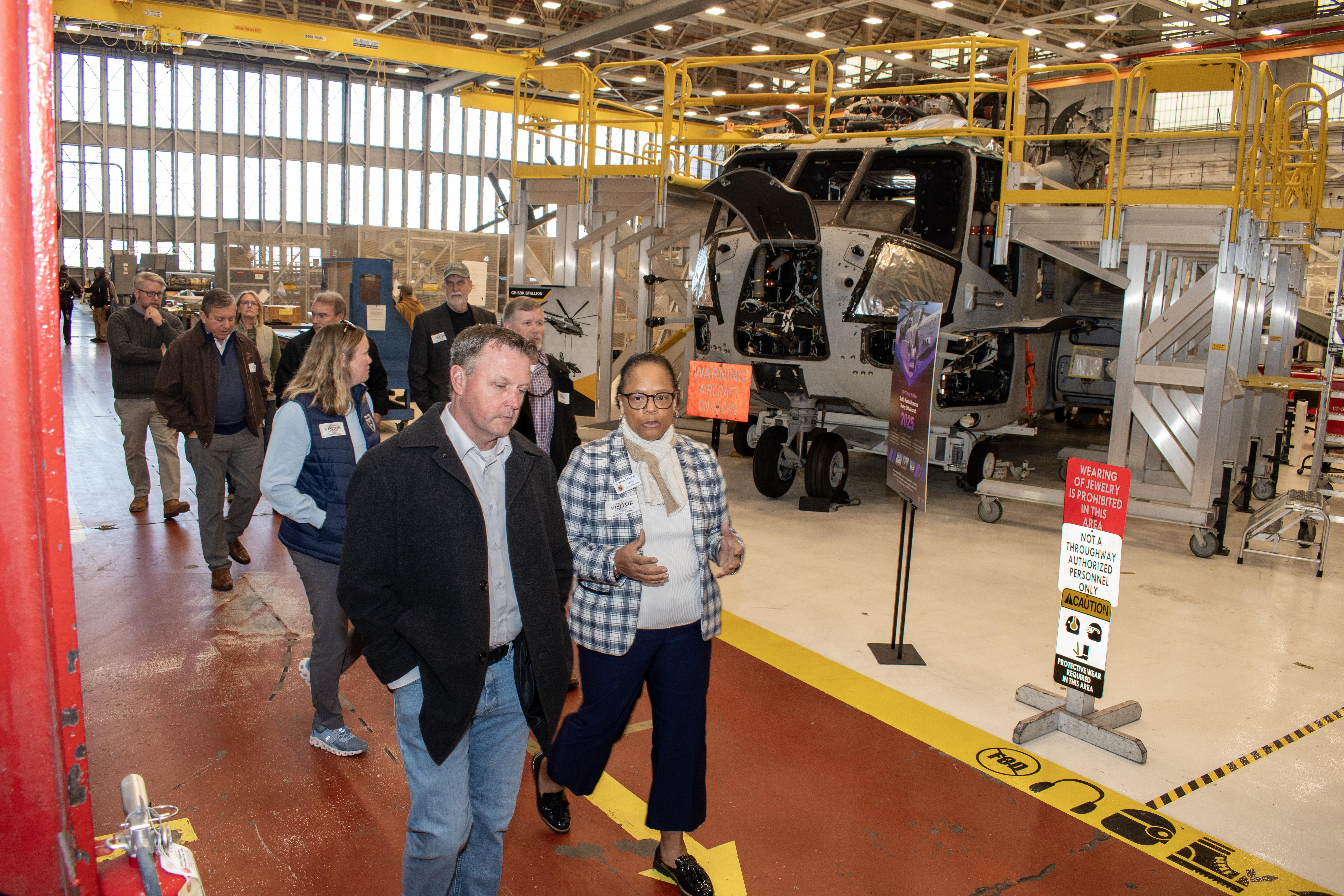 Group of people walk along a red isle in front of military aircraft inside aircraft hangar