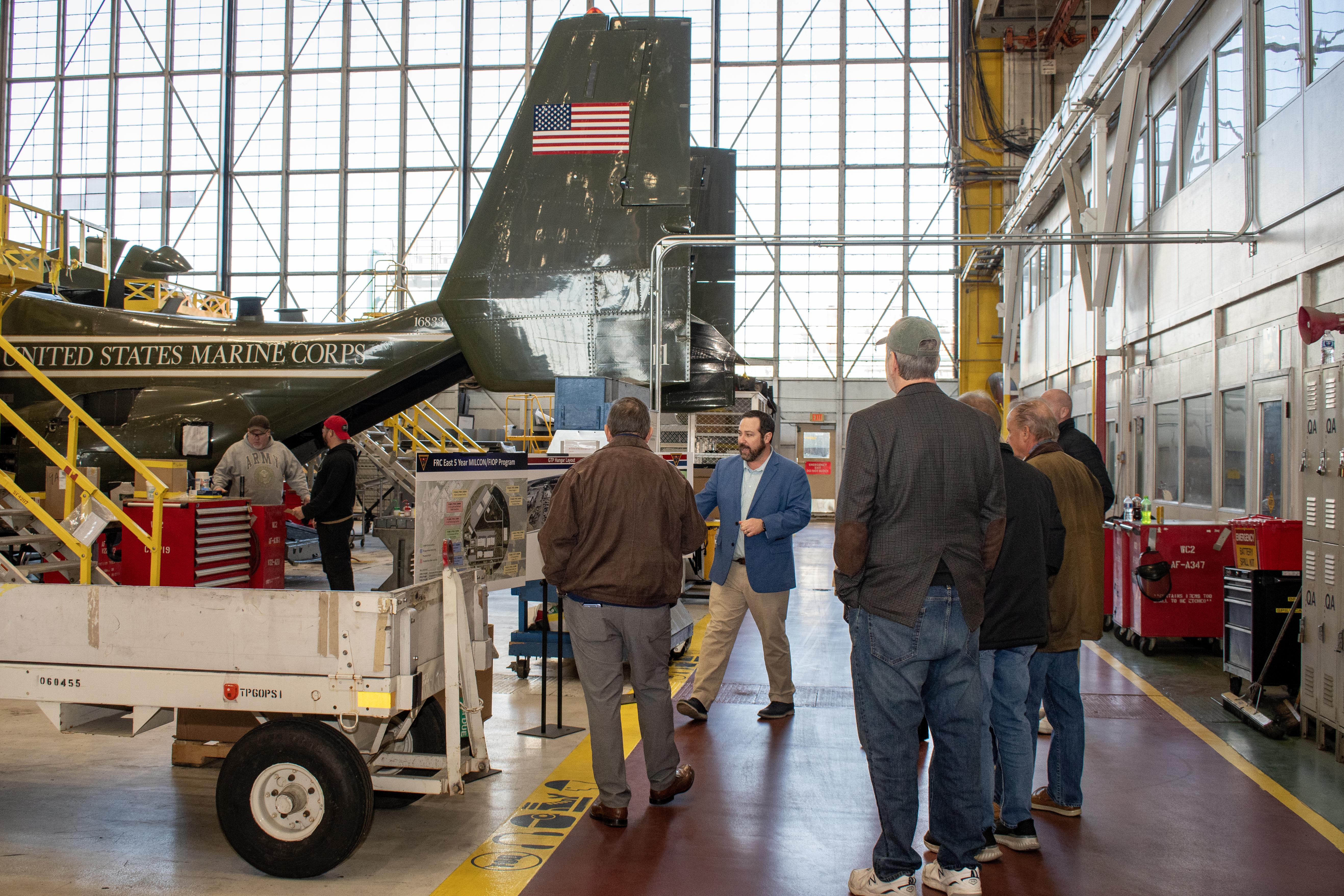 Group of people in aircraft hangar looking at the tail end of a V-22 Osprey