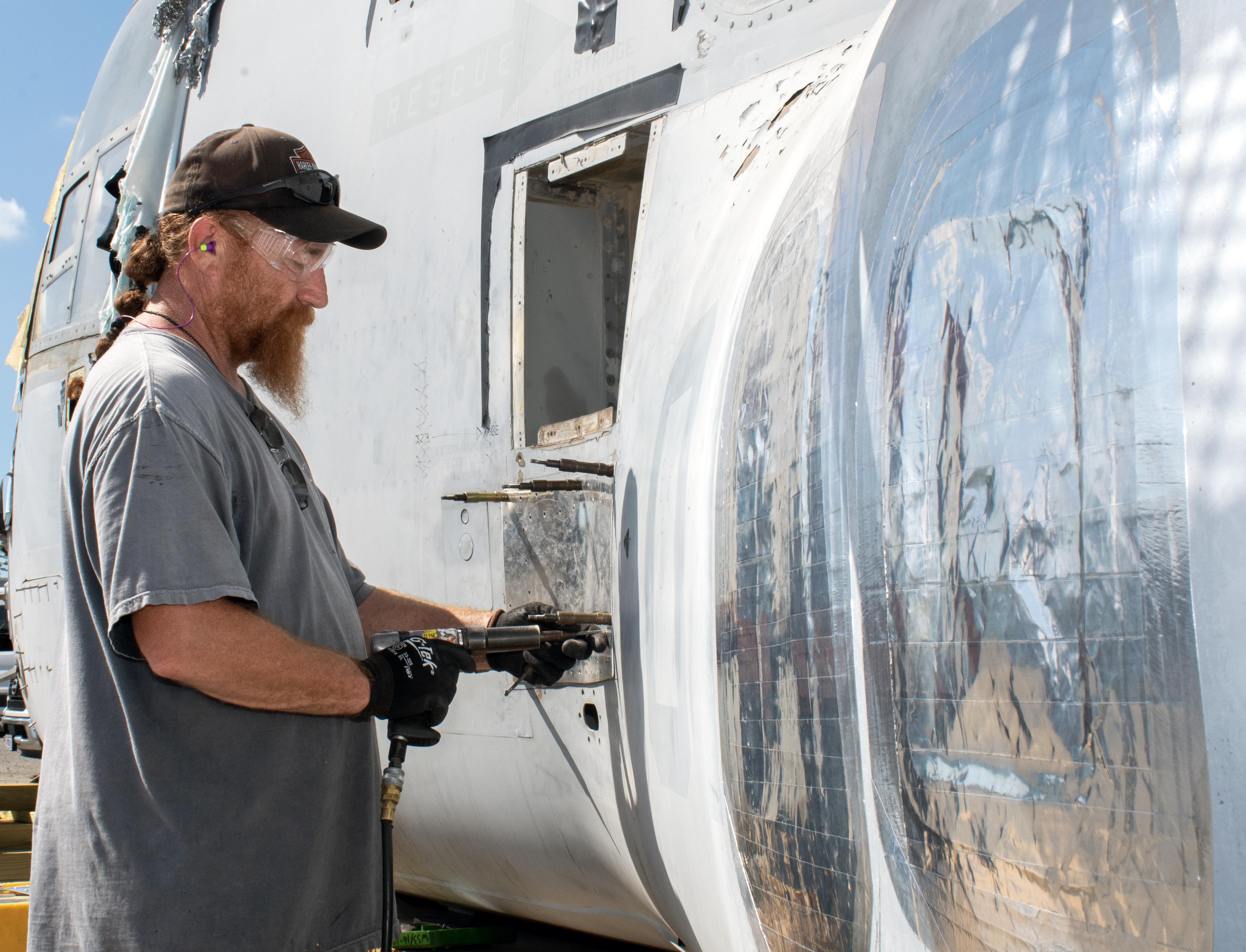 Man in grey shirt works on sheet metal on military aircraft exterior 
