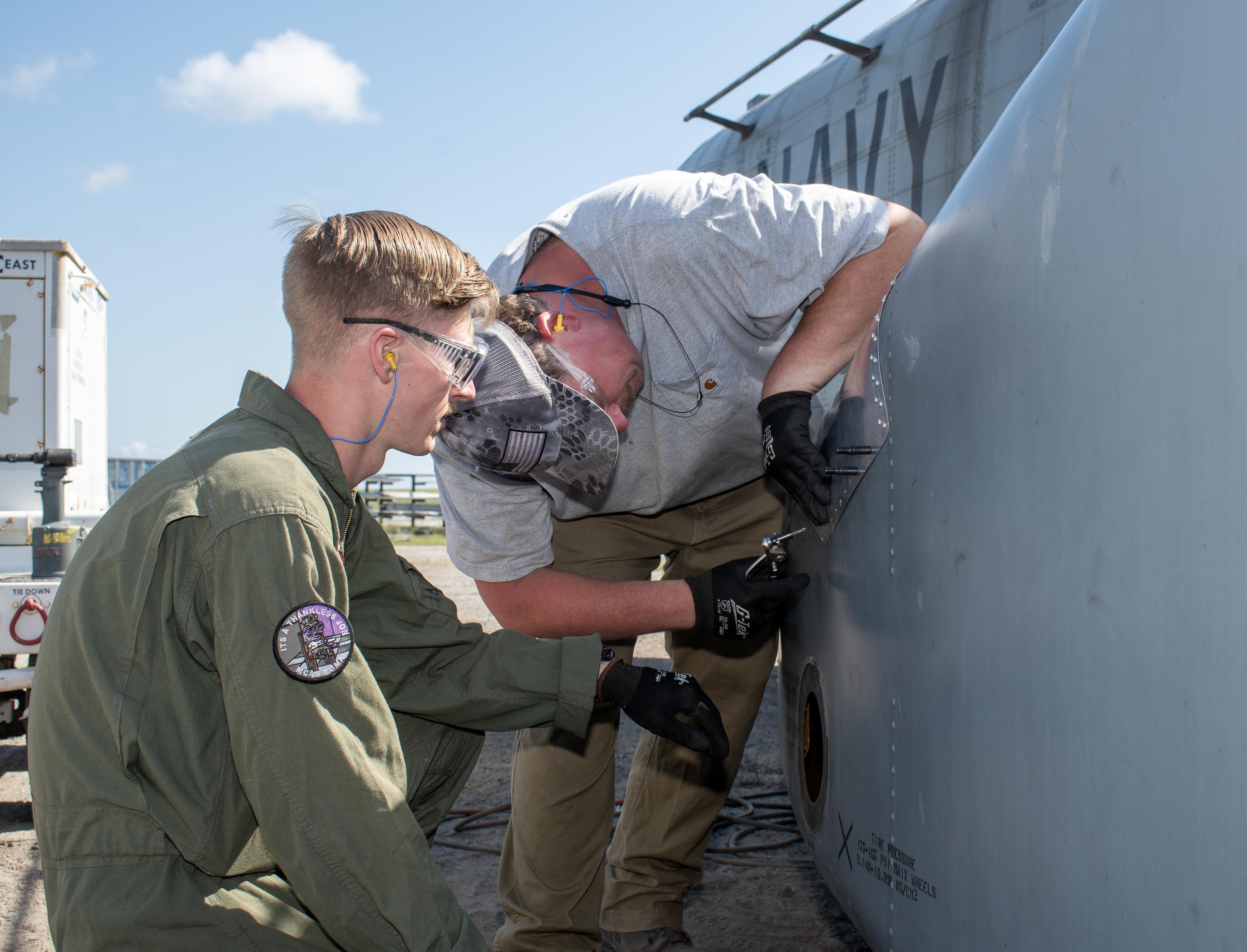 Marine and man in grey shirt work on exterior of military aircraft 