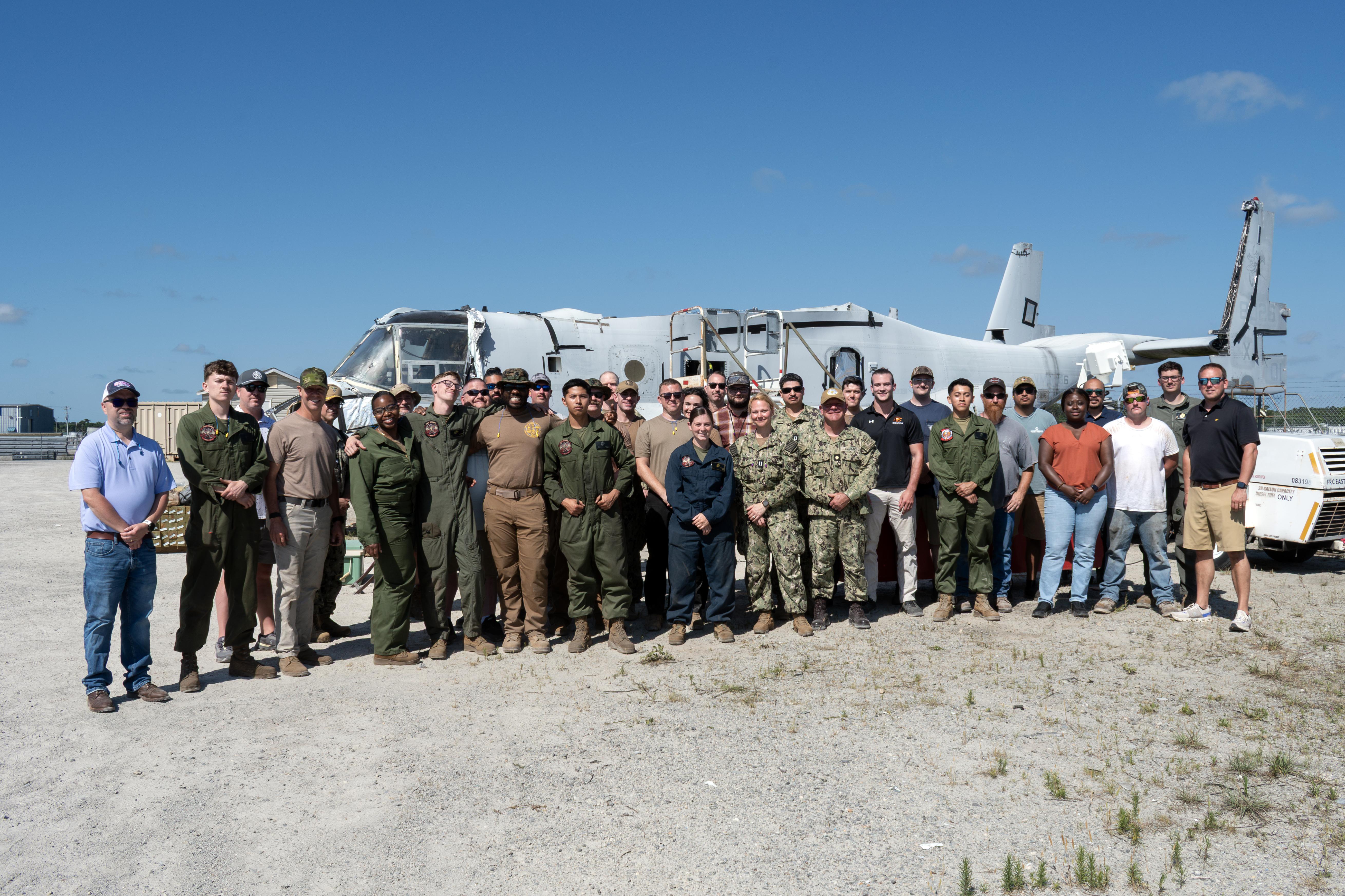 Group of civilians and service members pose for group photo in front of military aircraft