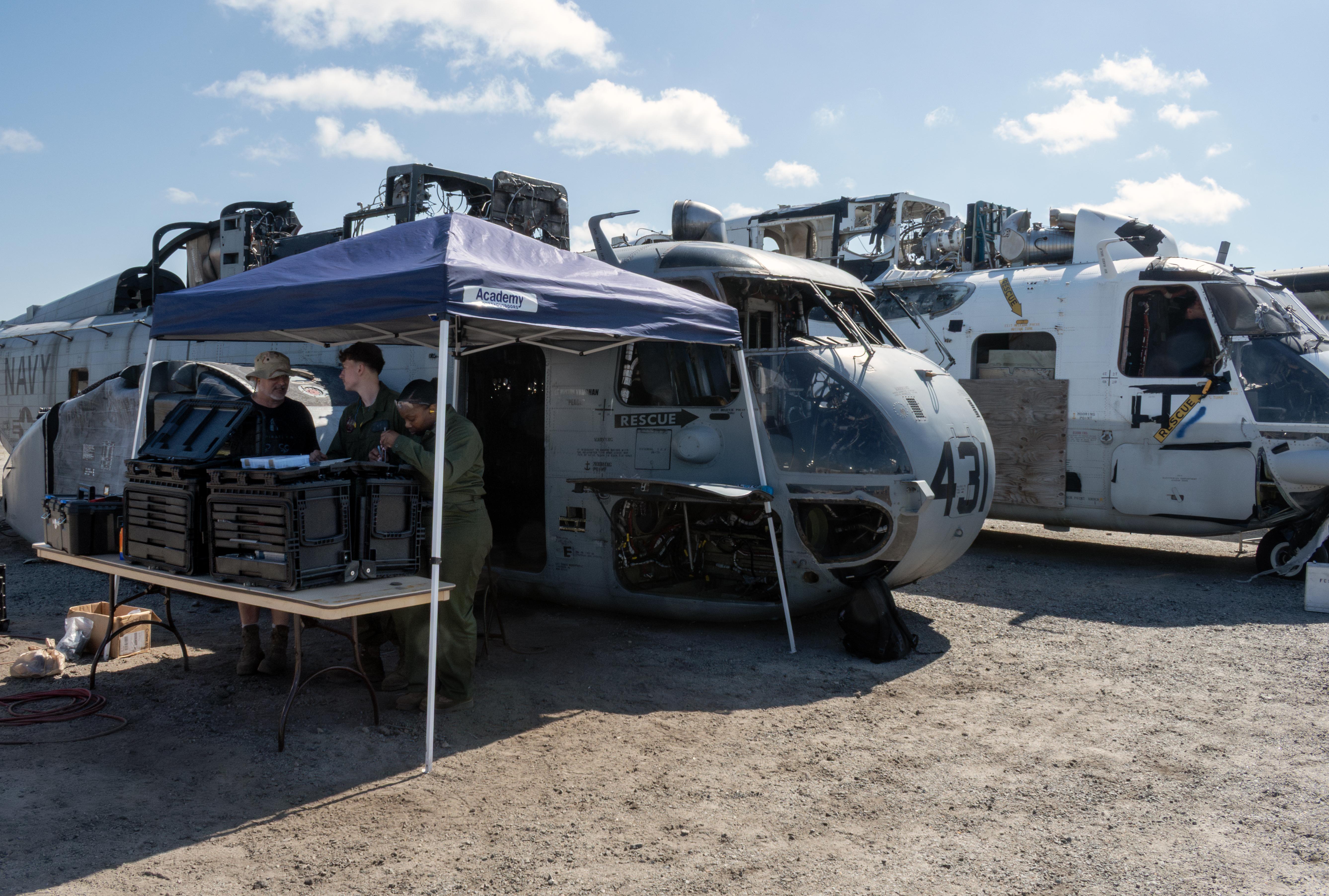 Three people stand under tent near two military aircraft 