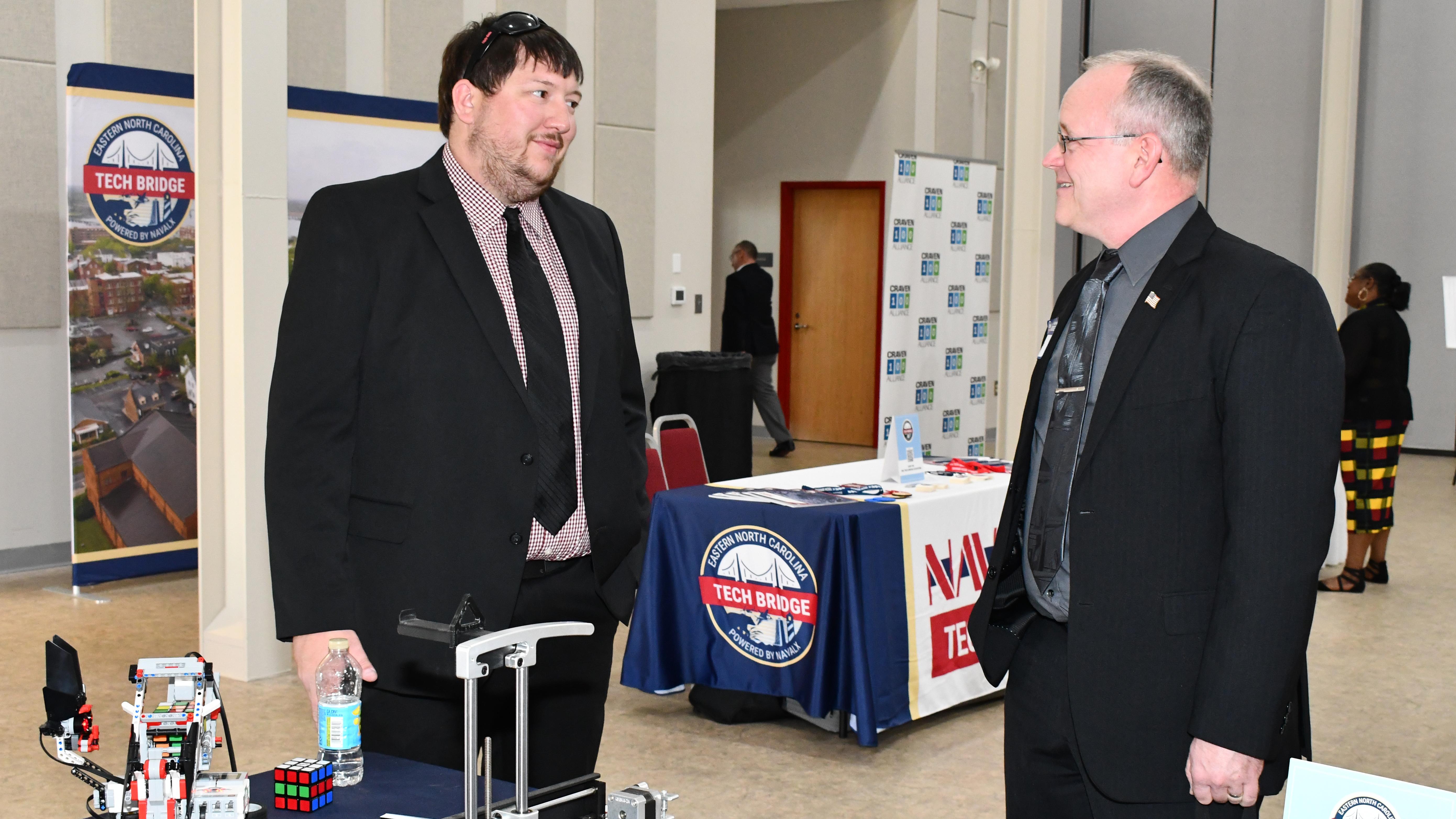Two men talk in front of expo table