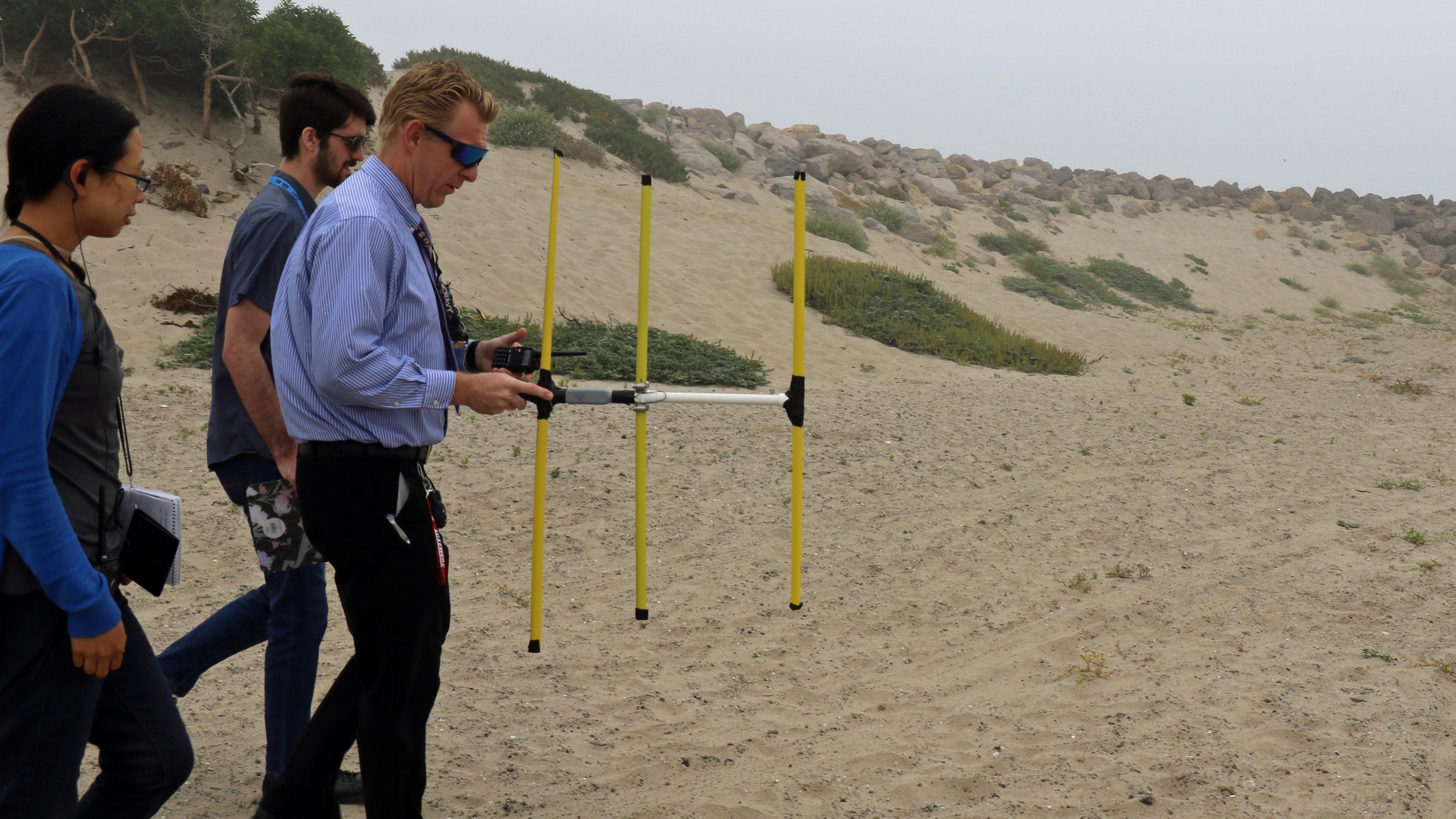 Diane Phung, Thomas Hentges, and Phillip Porter hunt for a transmitter hidden on the beach in Point Mugu, California, 