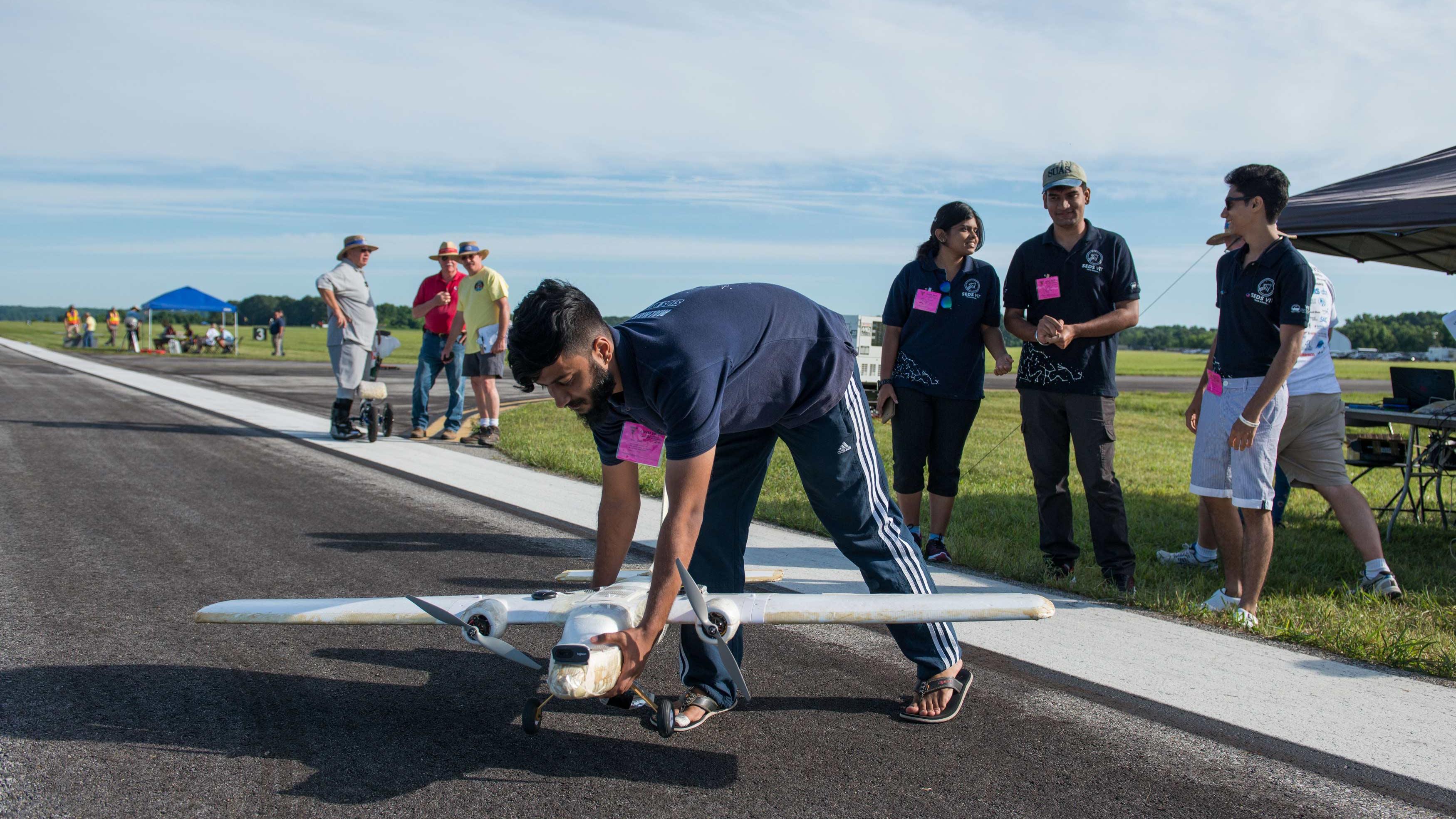 A student sets their small unmanned system on the flight line joined by his teammates and competition volunteers in the background.