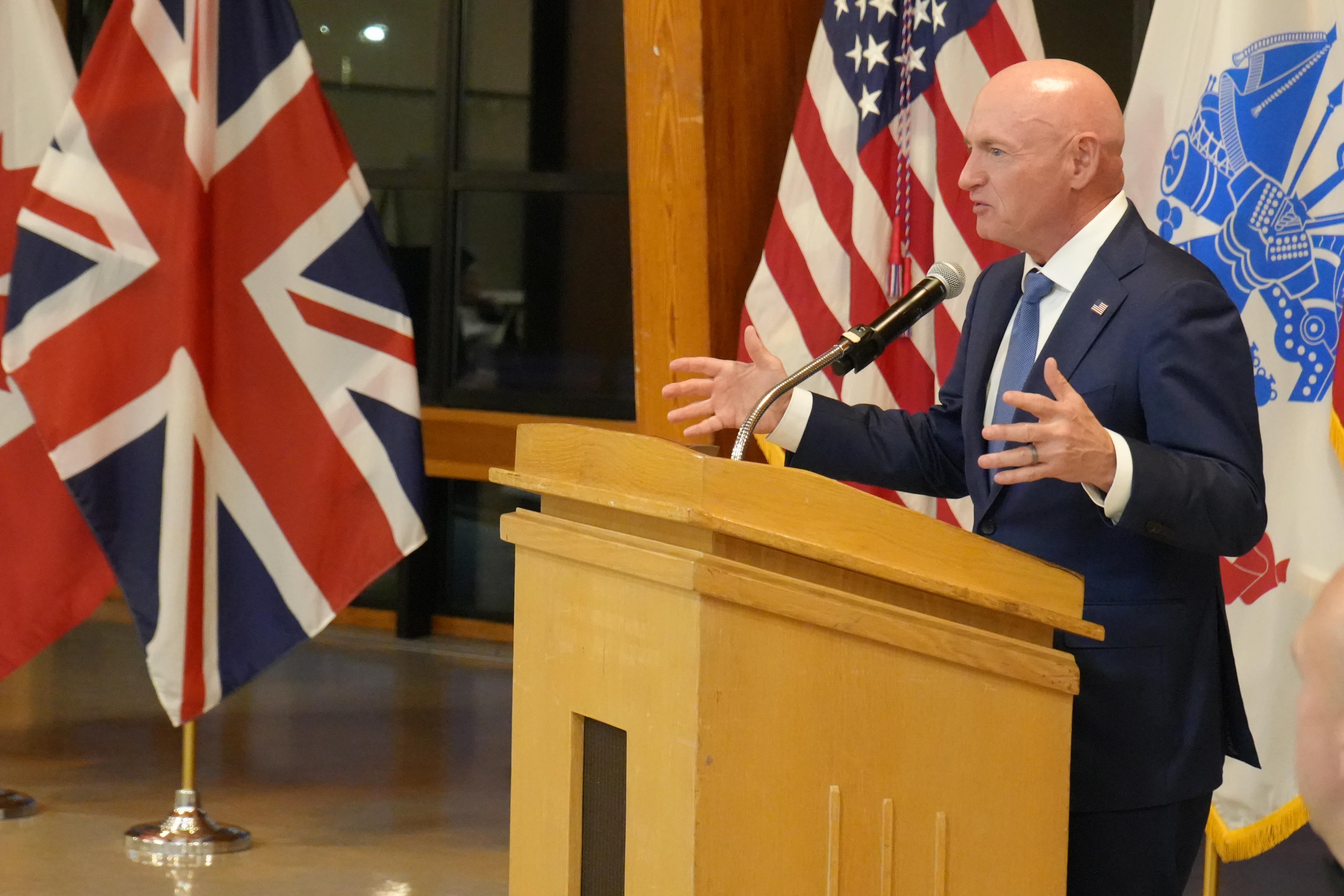 A speaker gives remarks at a podium in front of flags.
