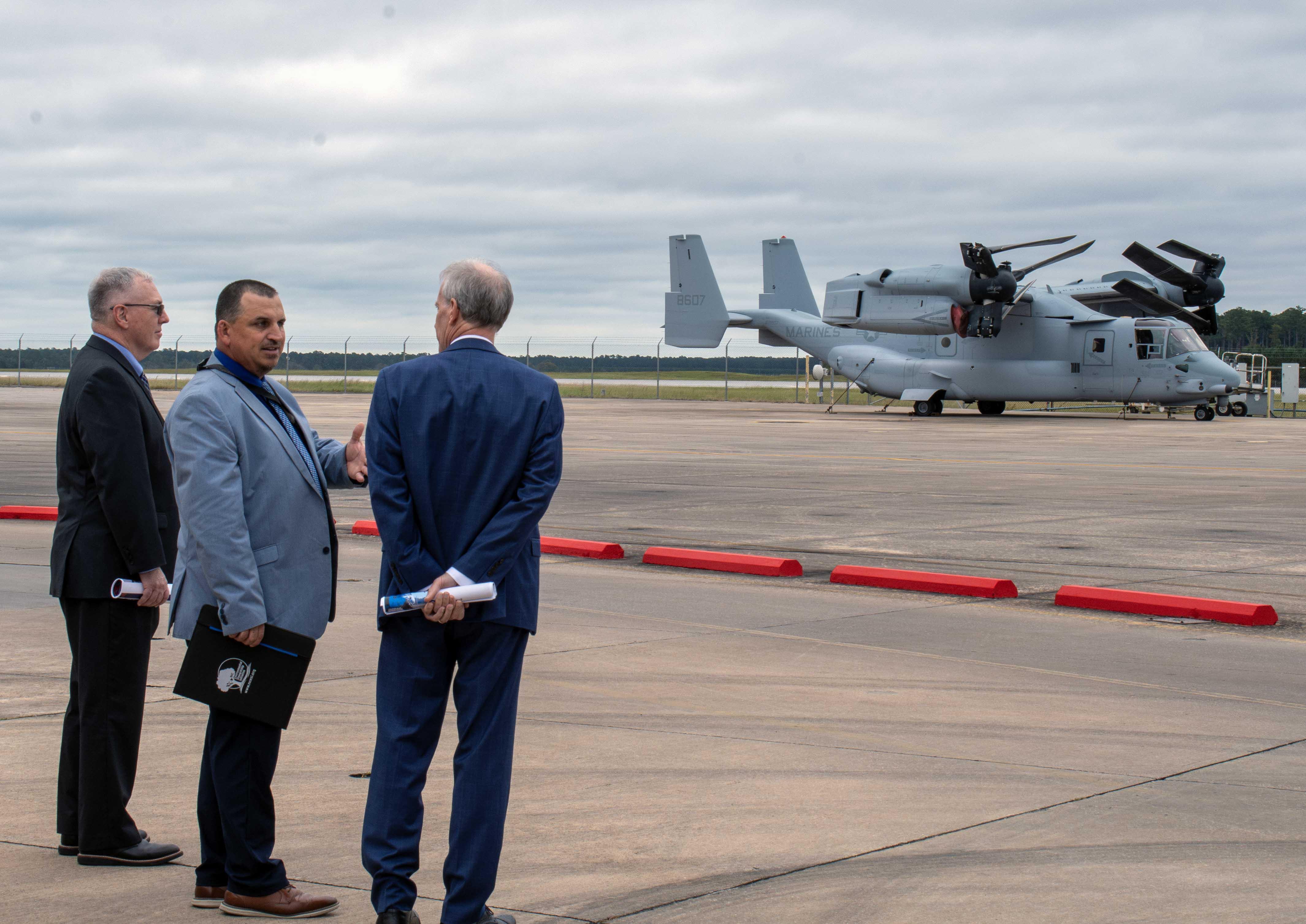 Three men stand outside in front of a military aircraft