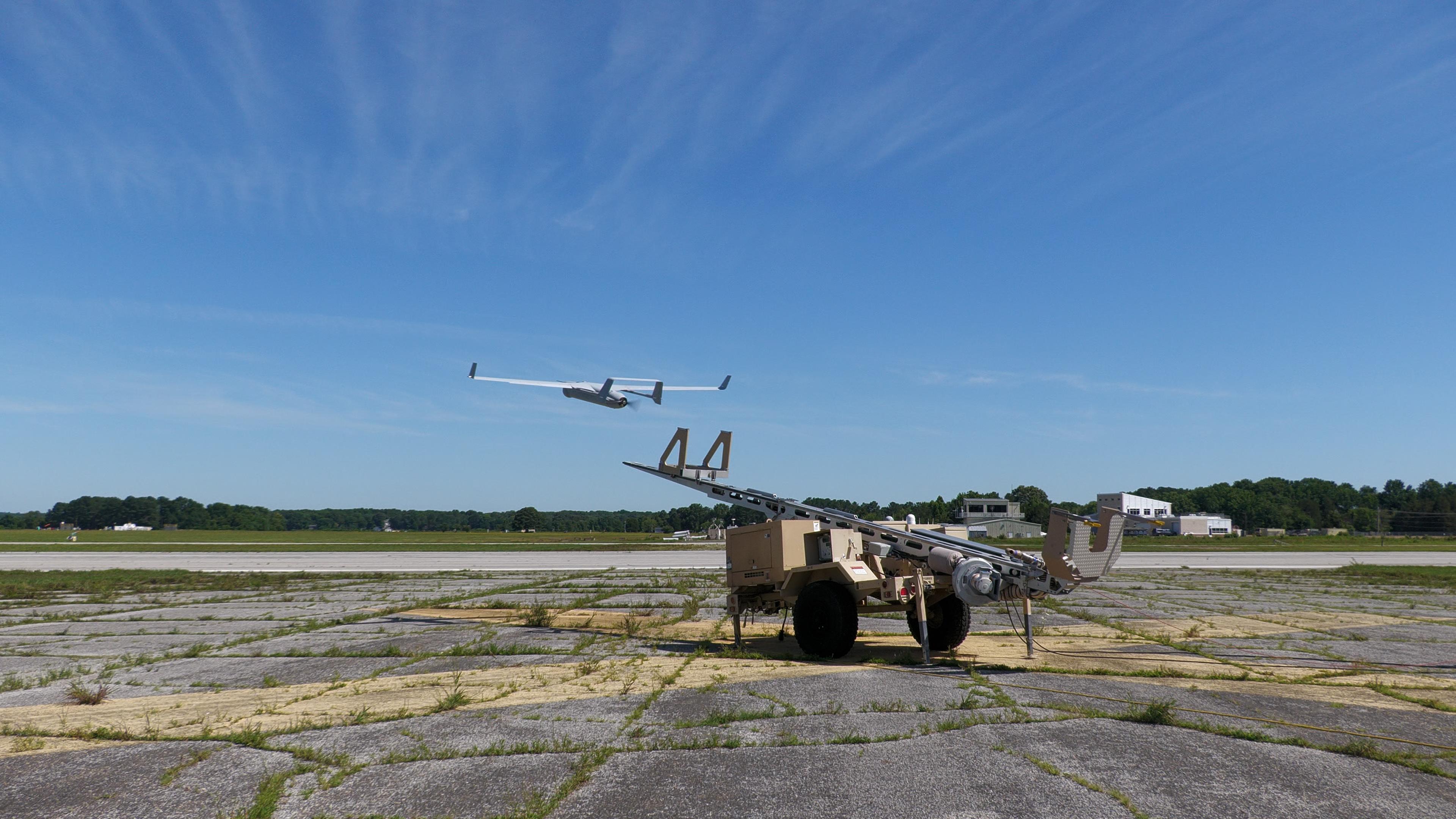 An RQ-21 Blackjack fixed-wing unmanned aerial system launches into blue skies over an airfield.