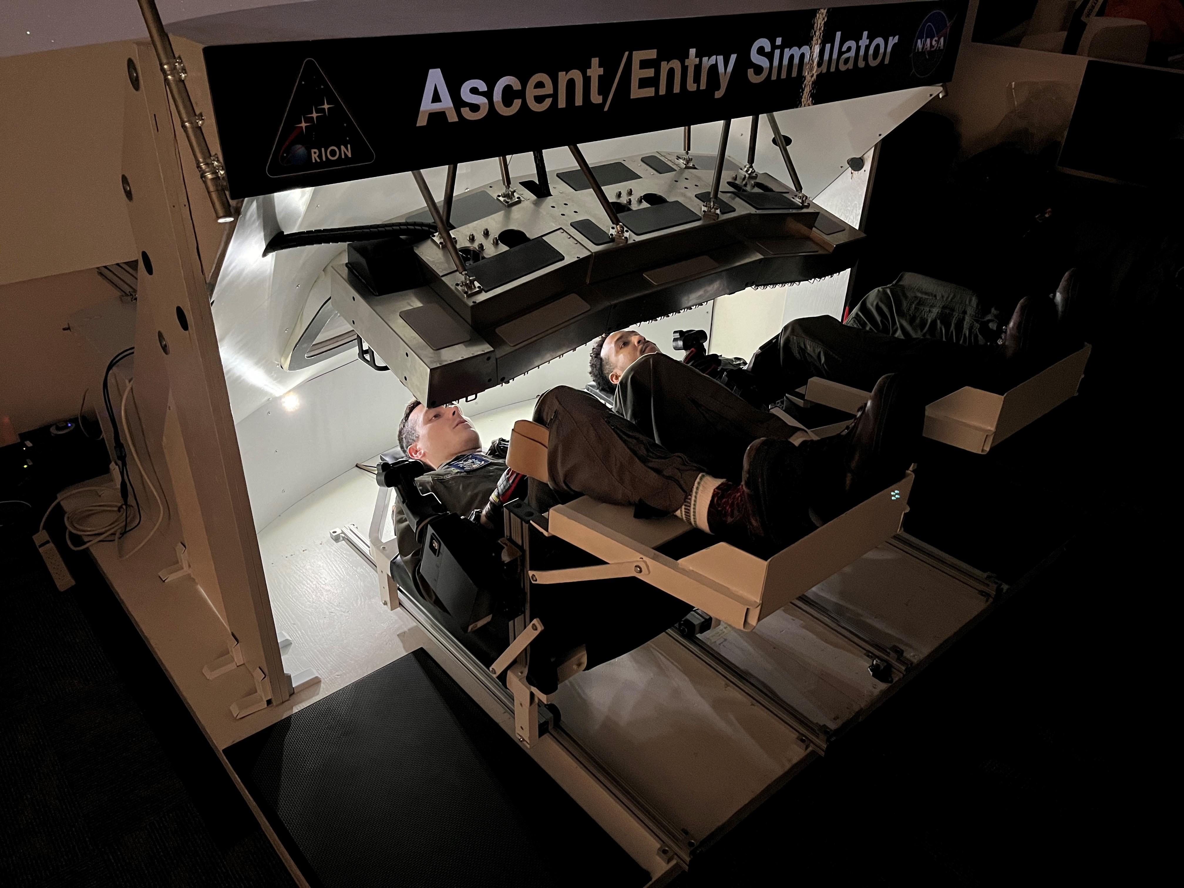 Two Navy pilots operate an Orion spacecraft display monitor.