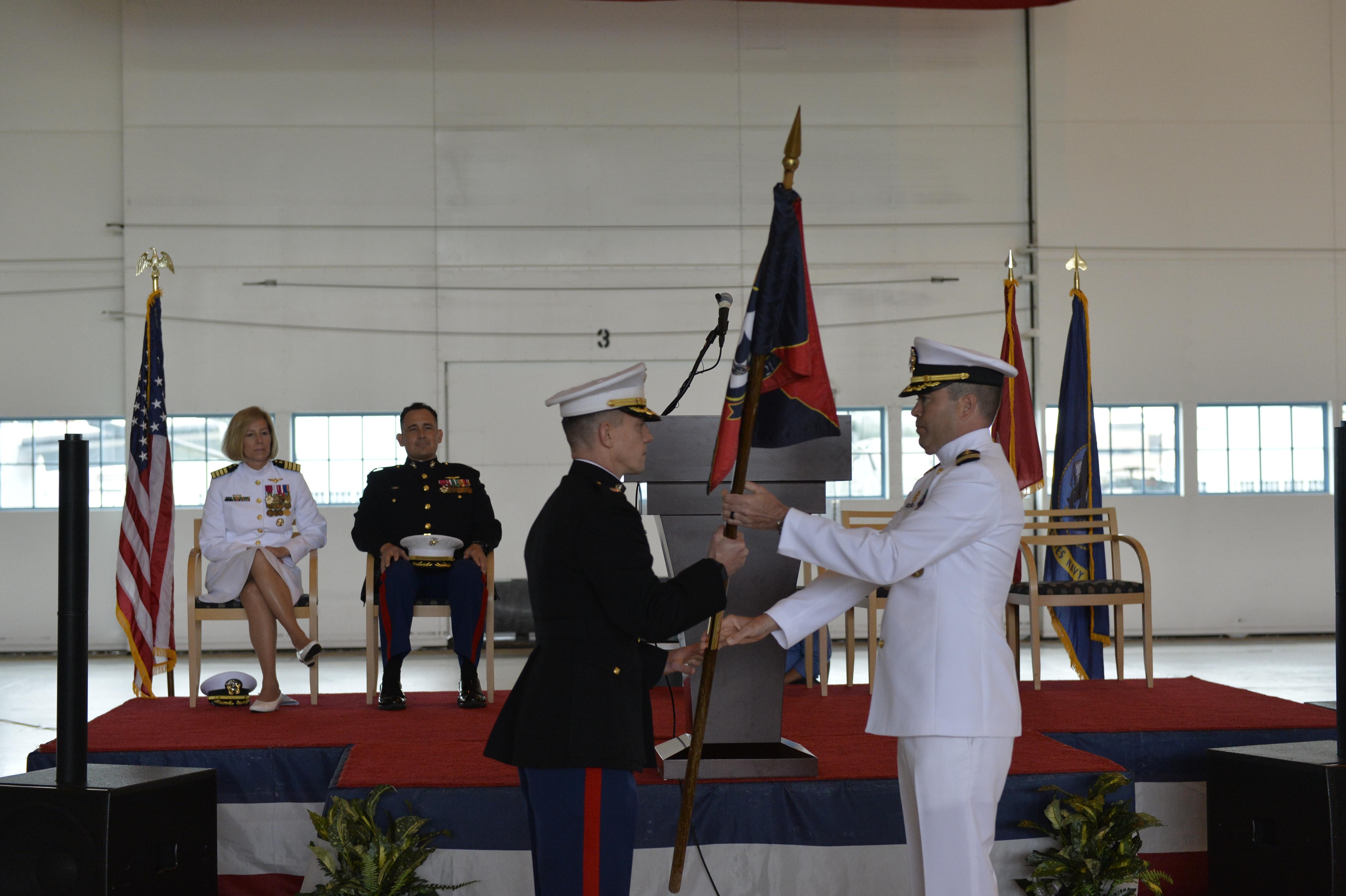 Lt. Col. Matthew Baumann takes a command flag from Cmdr. Daniel short in an aircraft hangar.