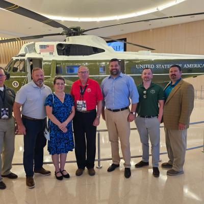A group of men and women stand in front of the VH-3D inside a building