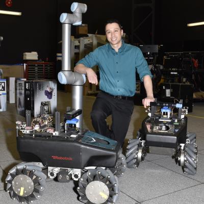Dr James Hing poses with robots in the Robotics and Intelligent Systems lab