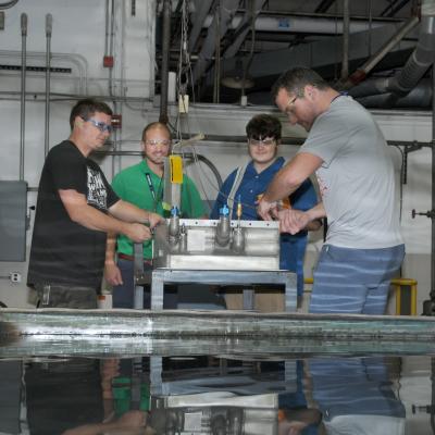 Artisans lower H-53 helicopter radiator into test pool to check for air leaks