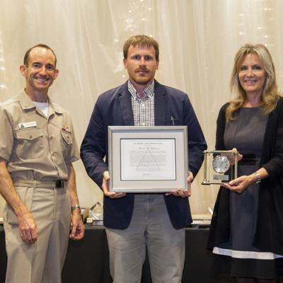 Aaron Lehman accepts the Dr. Manuel A. Garcia Memorial Award from Rear Adm. Scott Dillon, NAWCWD commander, and Joan Johnson, NAWCWD executive director, during the 2019 Honorary Awards Ceremony at China Lake on June 25. (U.S. Navy photo by Ryan Smith)