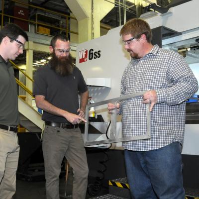 Men discuss metal bracket used in component production