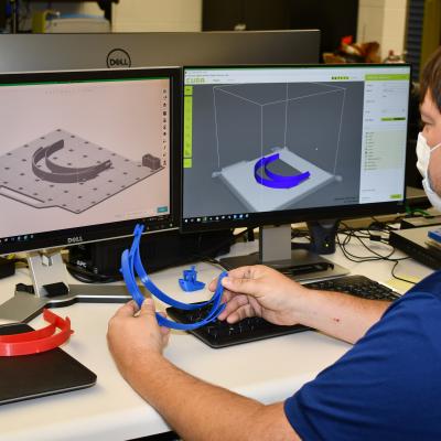 Man compares 3D-printed plastic headband to model on computer screen
