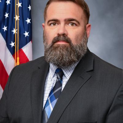 Professional headshot of man wearing a suit with the American flag in background 