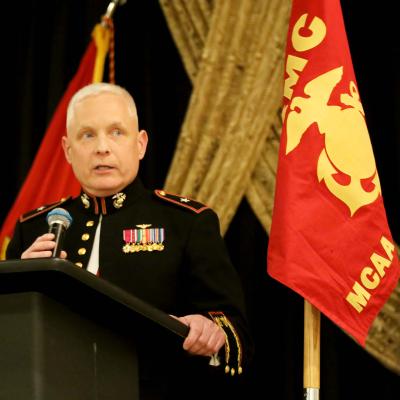 Man standing at a podium with a microphone in Marine Corps uniform