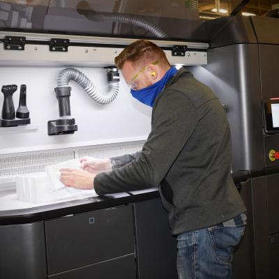 Fleet Readiness Center Southeast (FRCSE) Mechanical Engineer, Matthew Simon, removes excess nylon powder from 3D printed nasopharyngeal swab cages before going into an automated glass bead blaster for further processing. 