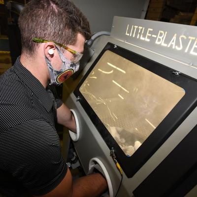 Fleet Readiness Center Southeast (FRCSE) Mechanical Engineer, Evan Grambling, utilizes a manual glass bead blaster as part of the processing procedures involved in the 3D printing of nasopharyngeal swabs. 