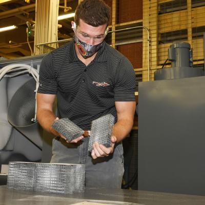 Fleet Readiness Center Southeast (FRCSE) Mechanical Engineer, Evan Grambling, removes 3D printed nasopharyngeal swab cages from the automated glass bead blaster after a timed blasting cycle.
