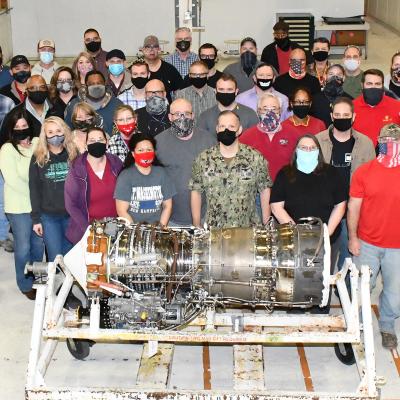 Group of aircraft workers poses for group photo behind T64 engine