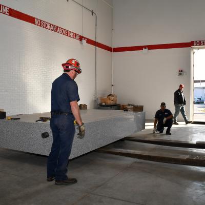 Rigging technicians move a granite table weighing 14 tons into place at Fleet Readiness Center East (FRCE). The table is part of a coordinate measuring machine (CMM). FRCE recently acquired two new CMMs capable of large-volume measurement. In addition to providing large item measurements, depot officials say these additional machines will improve efficiency and reduce wait times caused by maintenance and equipment calibration.