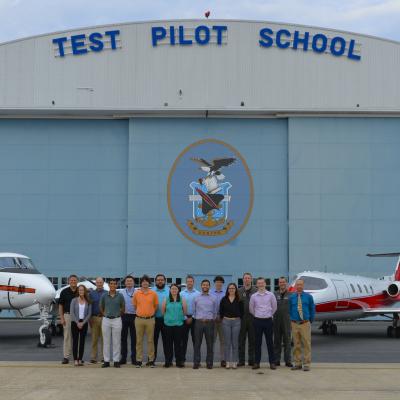 Civilian engineers from NAWCAD line up for a photo in front of U.S. Naval Test Pilot School's hangar in front of schoolhouse aircraft.