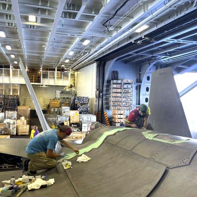 Two men repair F-35C Lightning II aircraft in hangar aboard aircraft carrier