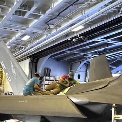 Two men repair F-35C Lightning II jet in hangar aboard aircraft carrier