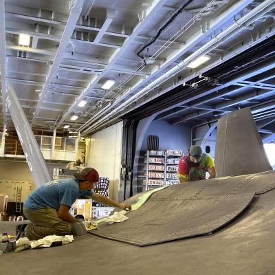 Two men repair F-35C Lightning II in hangar aboard aircraft carrier