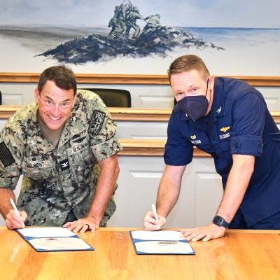 Two commanders look at camera while signing documents