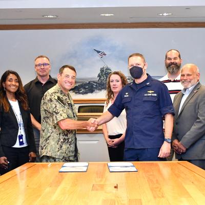 Group poses behind table as two commanders shake hands