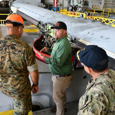 Fleet Readiness Center East (FRCE) V-22 Branch Head Andrew Rock, (center) briefs Maj. Gen. Scott F. Benedict, commanding general of 2nd Marine Aircraft Wing (MAW) and Capt. James Belmont, FRCE’s commanding officer, in front of the wing of an MV-22 Osprey.
