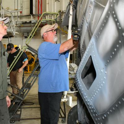 Fleet Readiness Center East (FRCE) H-53 Military Branch head and CH-53 pilot Capt. Ryan Boyer, left, and Aaron Bennett, an aircraft examiner at FRCE, conduct a flight control inspection on a tail pylon for a CH-53 helicopter.