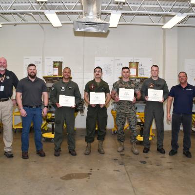 Terry Gerber, AV-8B Remote Visual Inspection (RVI) Program developer and manager, left, poses with graduates of the F402 Engine Tier 6 Inspector Rating certification course, Mar. 13, 2023. Launched in October of last year, this is the most recent course offered through the Fleet Readiness Center East’s AV-8B RVI program which trains and certifies Marines maintaining the AV-8B Harrier to successfully perform digital borescope processes on the Harrier’s F402 engine.
